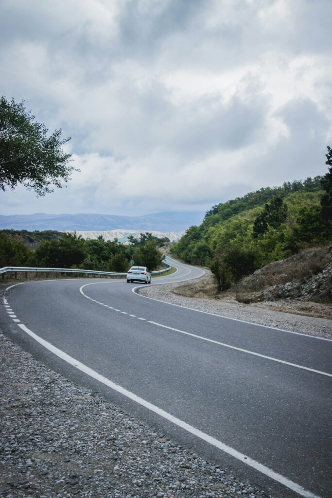 A car travelling along an open highway between green hills